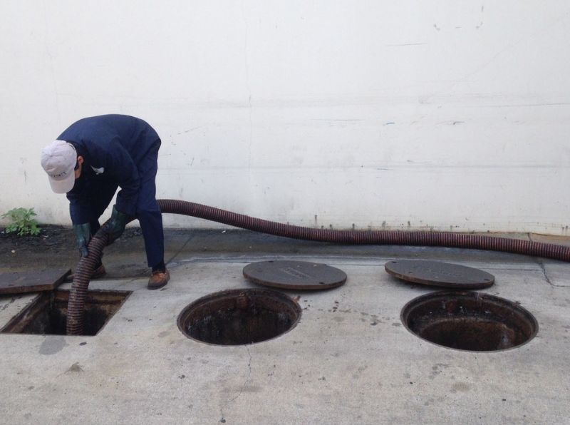 Technician pumping an outdoor grease interceptor with a vacuum hose