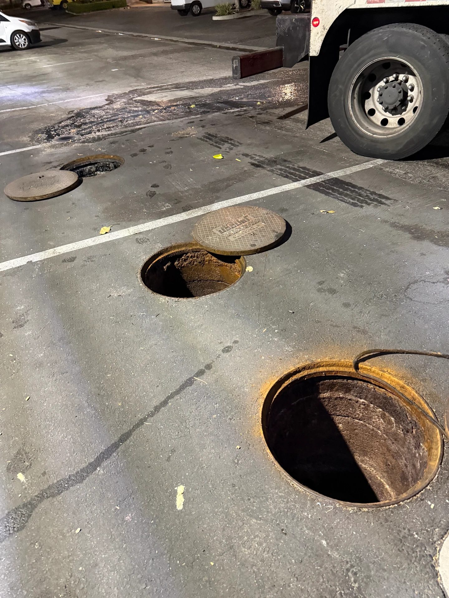 Outdoor in-ground grease interceptor lids opened next to a vacuum truck at night