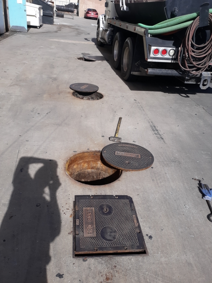 Daytime grease interceptor service with lids removed and vacuum truck staged in Banning, California
