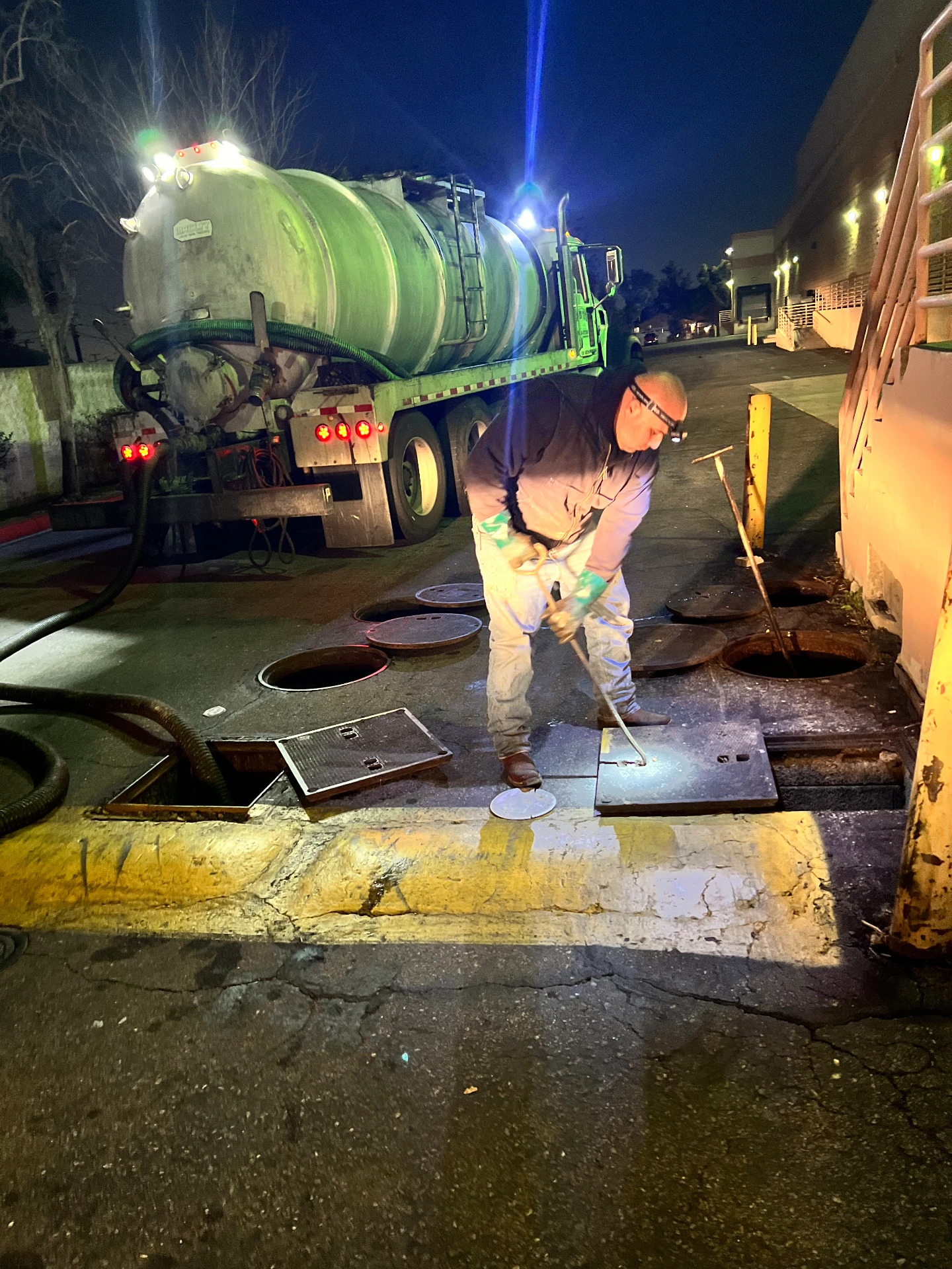 Night crew opening grease interceptor lids beside a vacuum truck in Banning, California