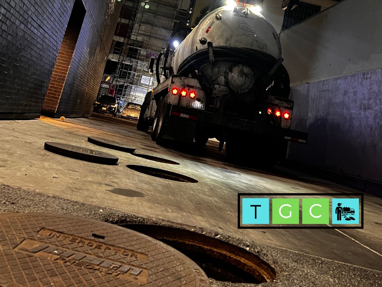Vacuum truck pumping a grease interceptor in a restaurant alley at night in Banning, California
